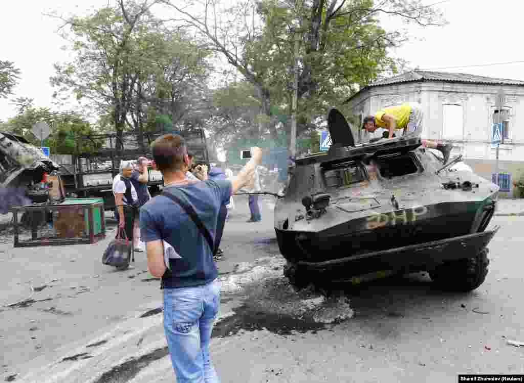 Местные жители фотографируют уничтоженный бронетранспортер, который принадлежал контролируемым Россией силам, захватившим в городе административные здания. Мариуполь, 13 июня.