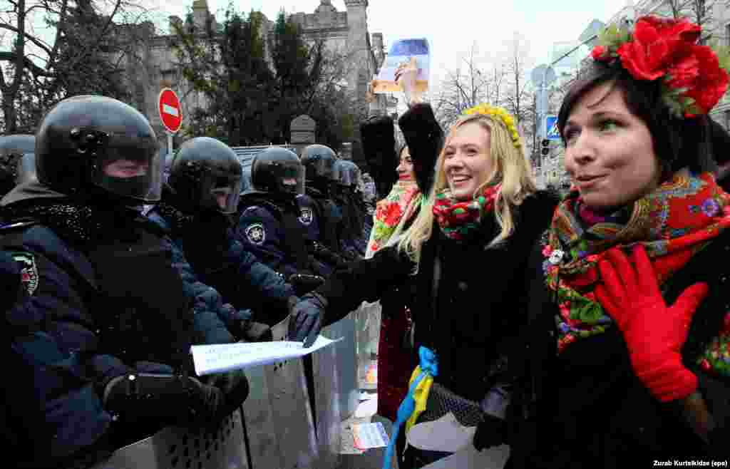 Ukrainian women, dressed in traditional costume, chat with riot police.